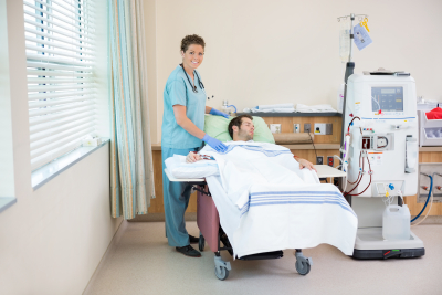 nurse smiling while standing by patient receiving renal dialysis in hospital room